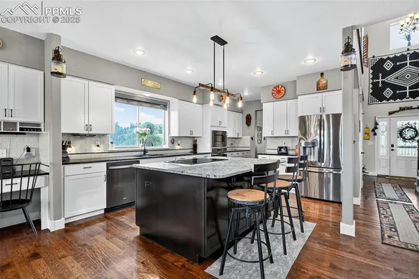 a kitchen with stainless steel appliances kitchen island granite countertop a sink a stove a refrigerator cabinets and chairs