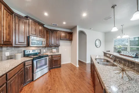 a kitchen with stainless steel appliances granite countertop wooden cabinets a sink dishwasher a stove and a refrigerator with wooden floor