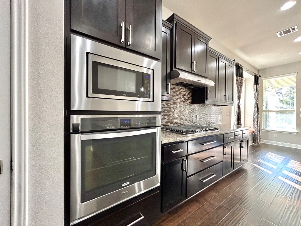 9313 Kyles Stake Road Austin, TX 78717 - Photo 10 of 40 Kitchen with stainless steel appliances, light stone countertops, backsplash, dark wood finished floors, and under cabinet range hood