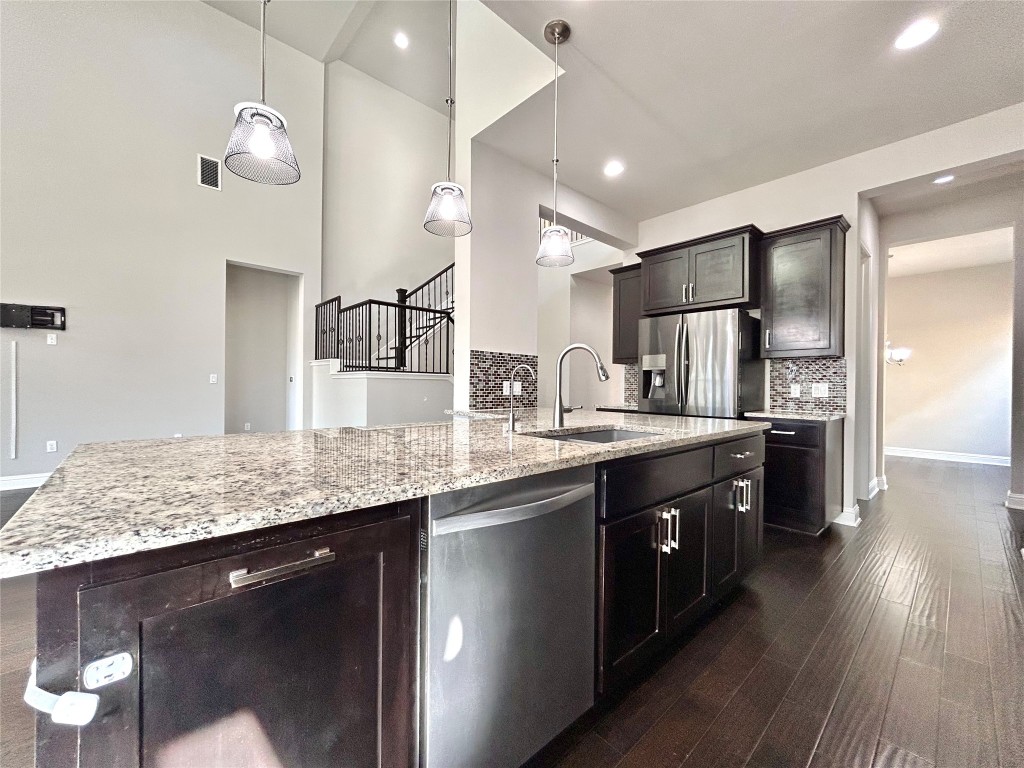 9313 Kyles Stake Road Austin, TX 78717 - Photo 8 of 40 Kitchen with dark wood-style flooring, appliances with stainless steel finishes, pendant lighting, light stone counters, and backsplash