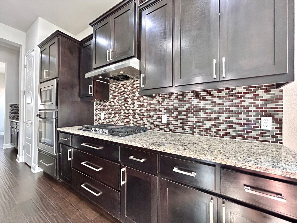 9313 Kyles Stake Road Austin, TX 78717 - Photo 9 of 40 Kitchen featuring light stone counters, appliances with stainless steel finishes, under cabinet range hood, and dark wood finished floors
