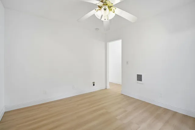 an empty room with a chandelier fan and wooden floor