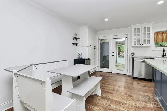 a large white kitchen with a refrigerator a sink dishwasher a stove and a dining table with wooden floor