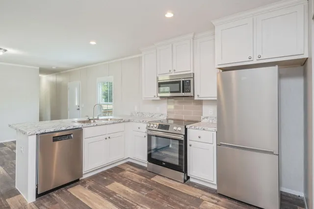 a kitchen with stainless steel appliances granite countertop a refrigerator a stove top oven a sink and dishwasher with wooden floor