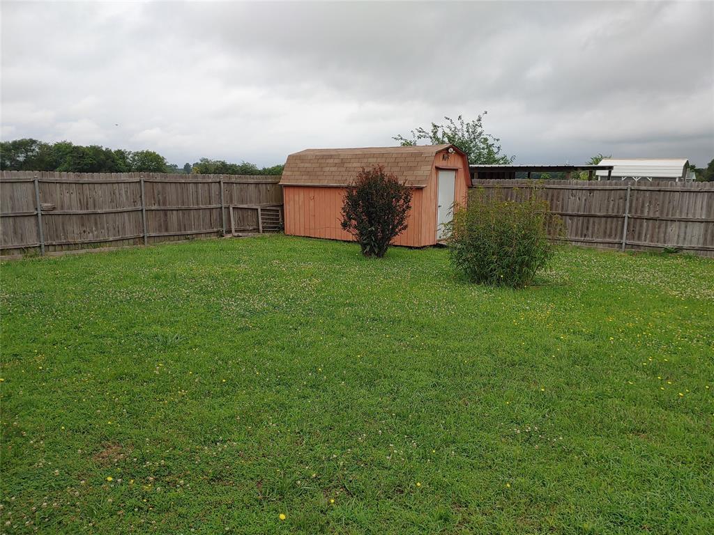 836 Airport Road Reno, TX 75462 - Photo 30 of 30 Expansive backyard featuring a privacy fence, a storage shed with a gambrel roof, and established shrubbery