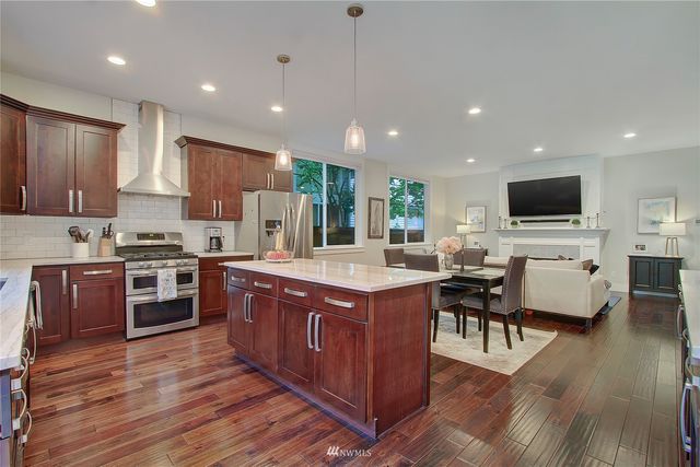 a kitchen with stainless steel appliances granite countertop wooden cabinets a sink a stove a dining table and chairs