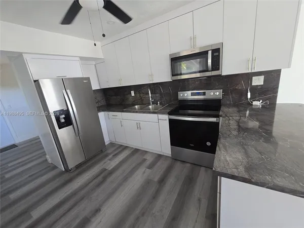 a kitchen with stainless steel appliances granite countertop a refrigerator a microwave a sink and white cabinets