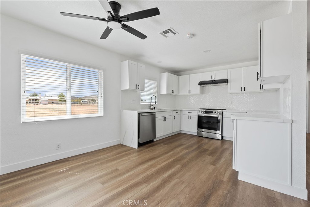20631 Zuni Road Apple Valley, CA 92307 - Photo 9 of 25 a kitchen with stainless steel appliances white cabinets a sink a stove a refrigerator and island with wooden floor