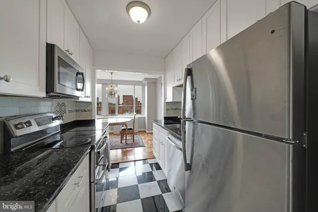 a kitchen with granite countertop a refrigerator a sink and white cabinets