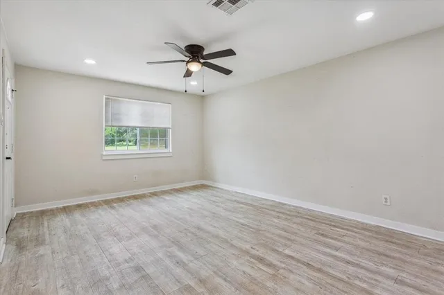an empty room with wooden floor fan and windows