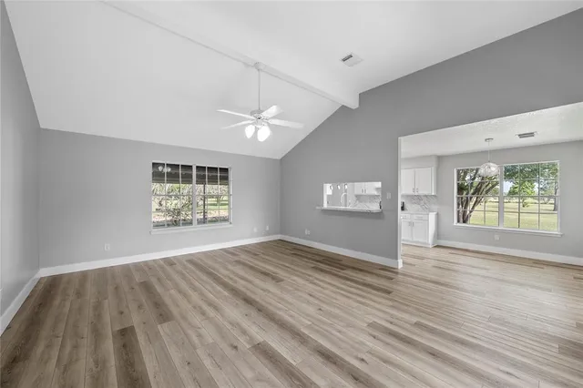 an empty room with wooden floor chandelier fan and windows