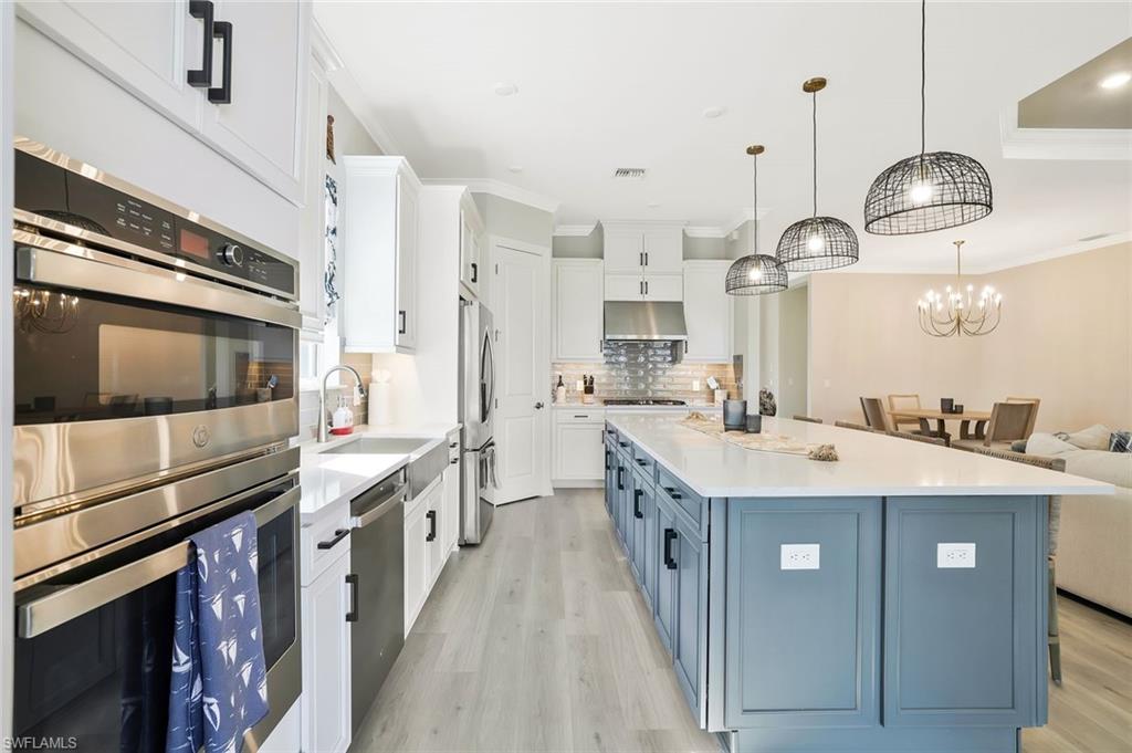 15804 Derna Street Naples, FL 34114 - Photo 10 of 28 Kitchen with stainless steel appliances, white cabinets, blue cabinets, light wood-style floors, and ornamental molding
