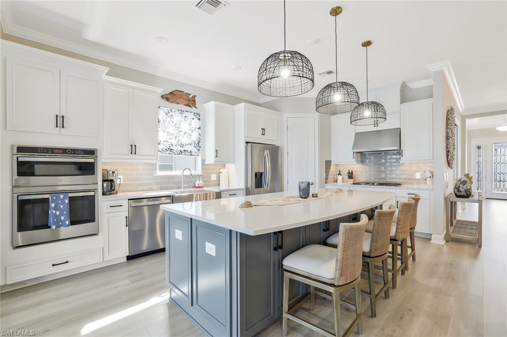 15804 Derna Street Naples, FL 34114 - Photo 11 of 28 Kitchen featuring white cabinets, ornamental molding, a kitchen island, and a breakfast bar area