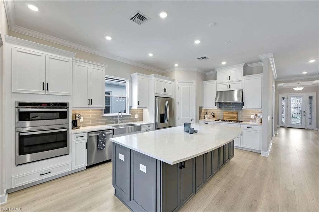 15804 Derna Street Naples, FL 34114 - Photo 7 of 22 Kitchen featuring crown molding, white cabinetry, a center island, appliances with stainless steel finishes, and light stone countertops