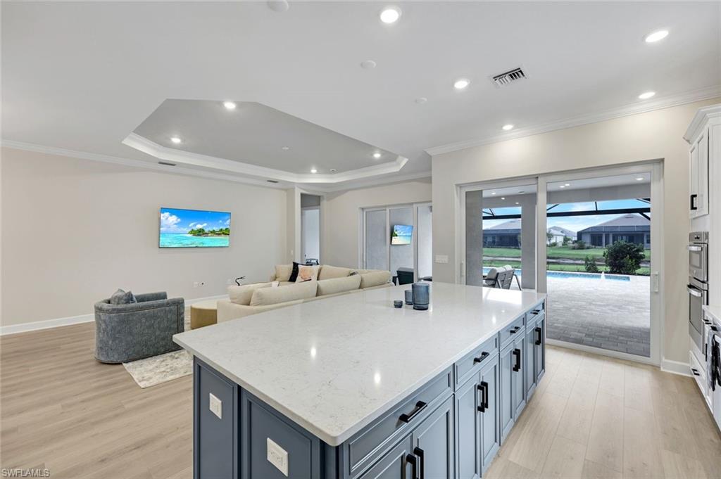 15804 Derna Street Naples, FL 34114 - Photo 22 of 22 Kitchen with light stone countertops, ornamental molding, open floor plan, a kitchen island, and light wood-type flooring