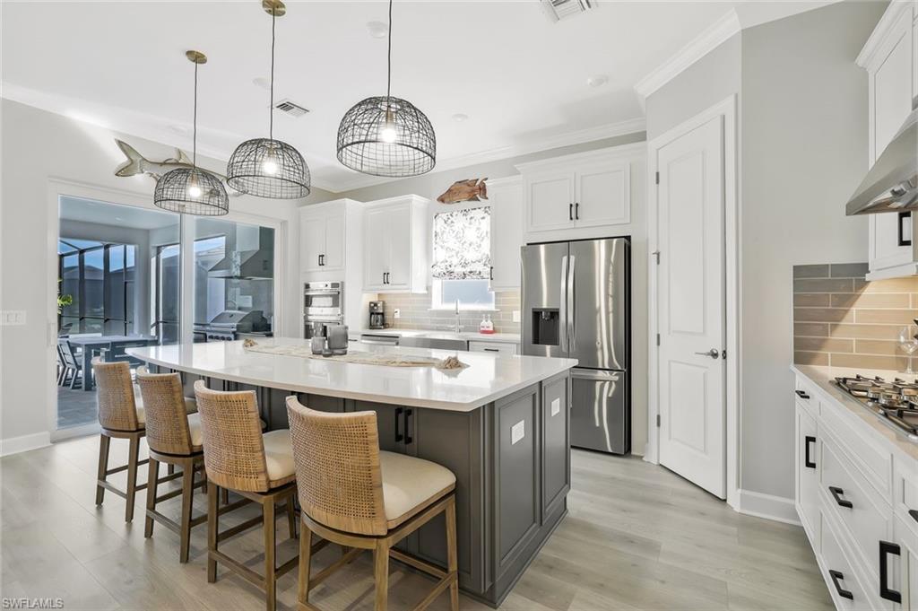 15804 Derna Street Naples, FL 34114 - Photo 9 of 28 Kitchen with a breakfast bar area, appliances with stainless steel finishes, white cabinets, pendant lighting, and a kitchen island
