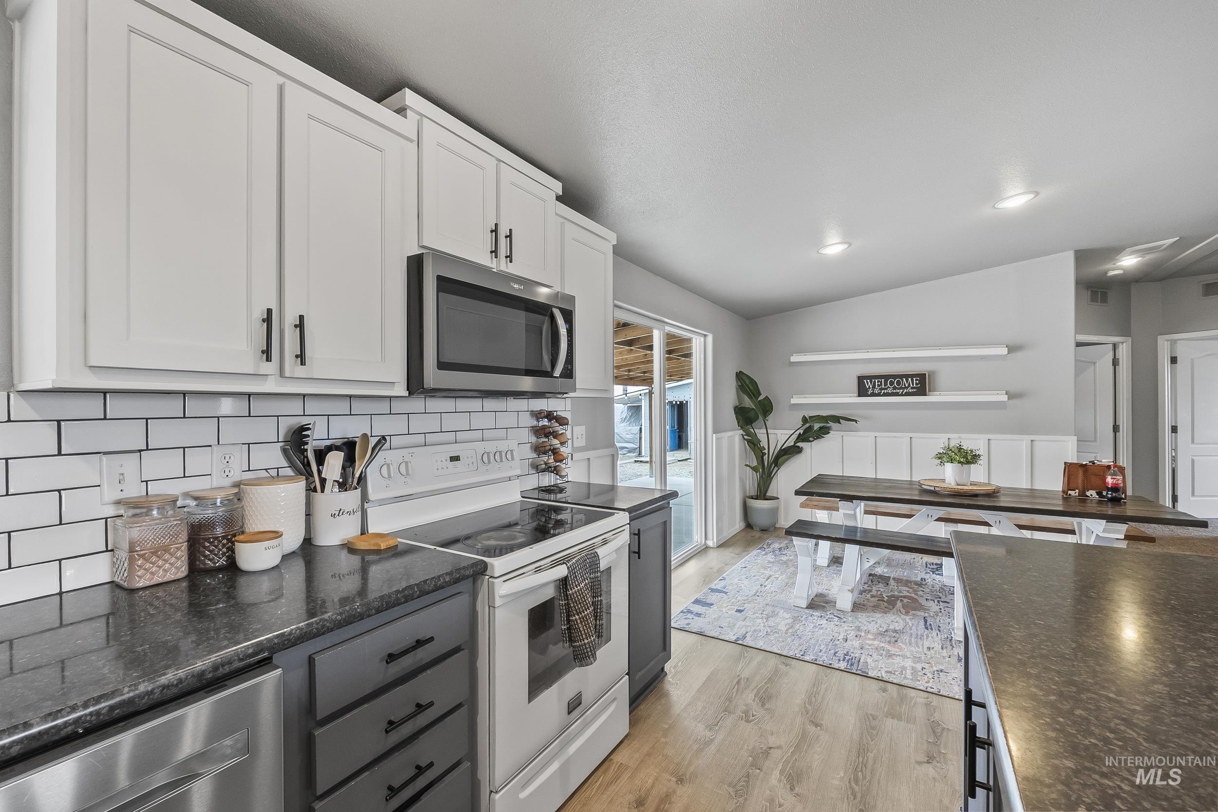 12944 Goodson Road Caldwell, ID 83607 - Photo 12 of 47 Kitchen with appliances with stainless steel finishes, white cabinets, lofted ceiling, dark stone countertops, and light wood-style flooring