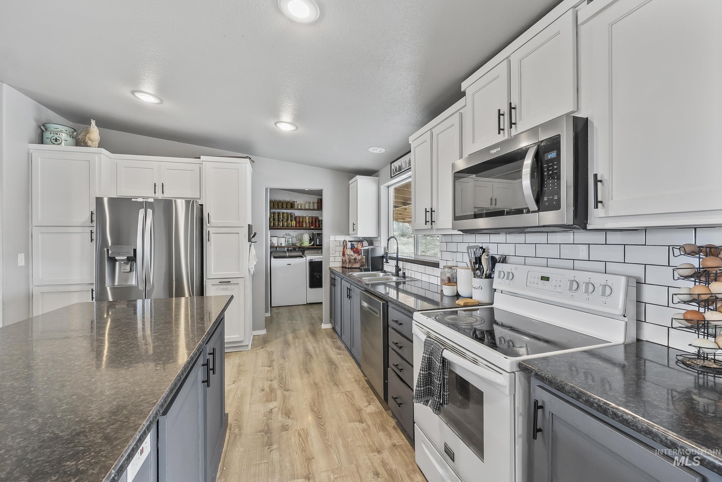 12944 Goodson Road Caldwell, ID 83607 - Photo 13 of 47 Kitchen with appliances with stainless steel finishes, white cabinets, vaulted ceiling, dark stone countertops, and gray cabinetry
