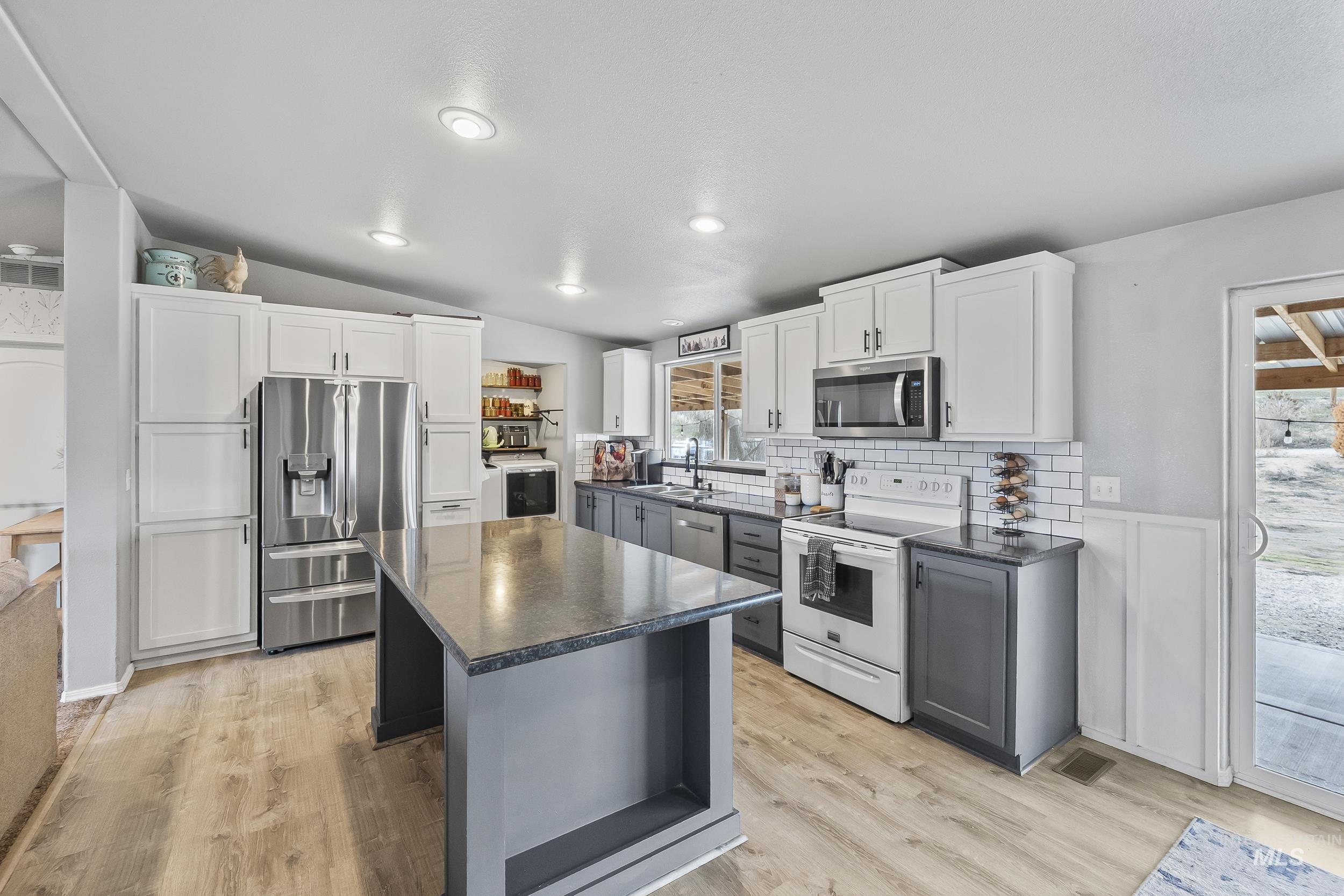 12944 Goodson Road Caldwell, ID 83607 - Photo 16 of 47 Kitchen featuring white cabinetry, gray cabinets, appliances with stainless steel finishes, light wood-style floors, and vaulted ceiling