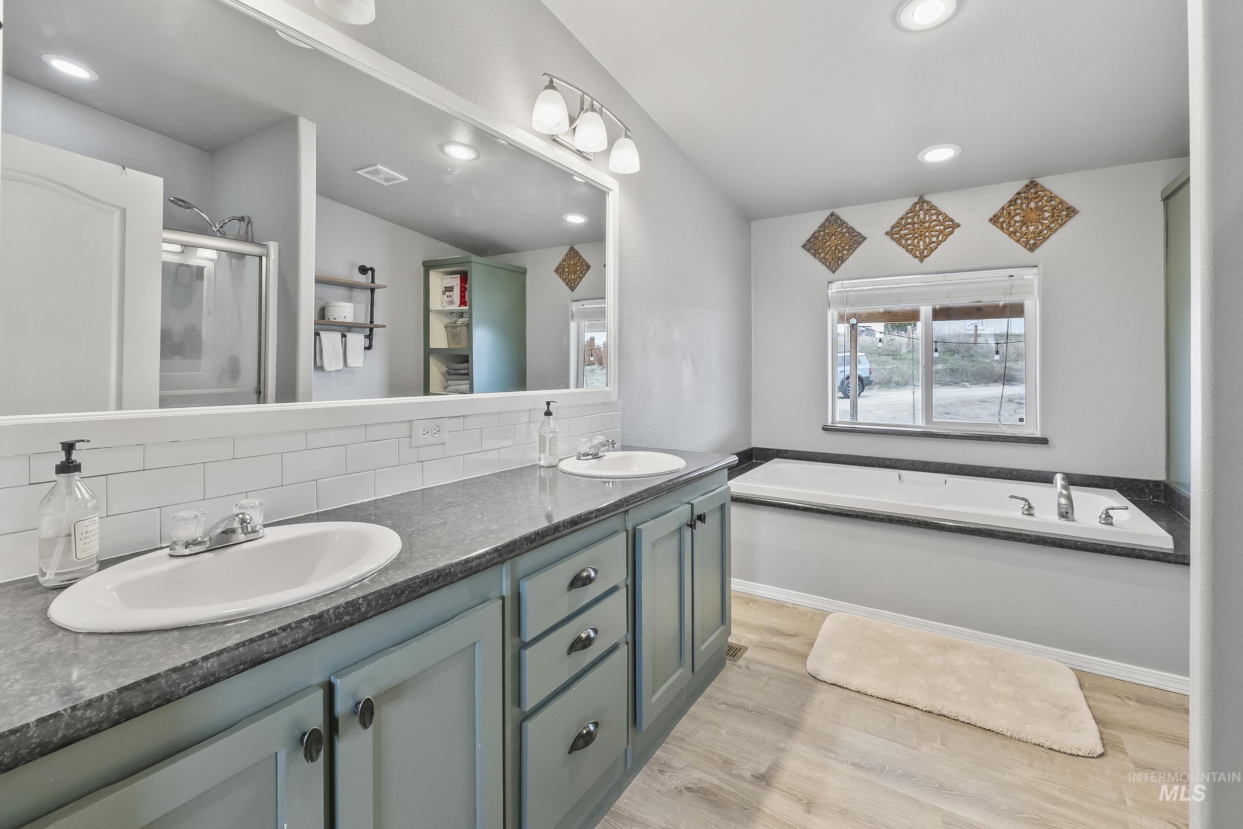 12944 Goodson Road Caldwell, ID 83607 - Photo 19 of 47 Bathroom with a shower stall, double vanity, light wood-style floors, a garden tub, and tasteful backsplash