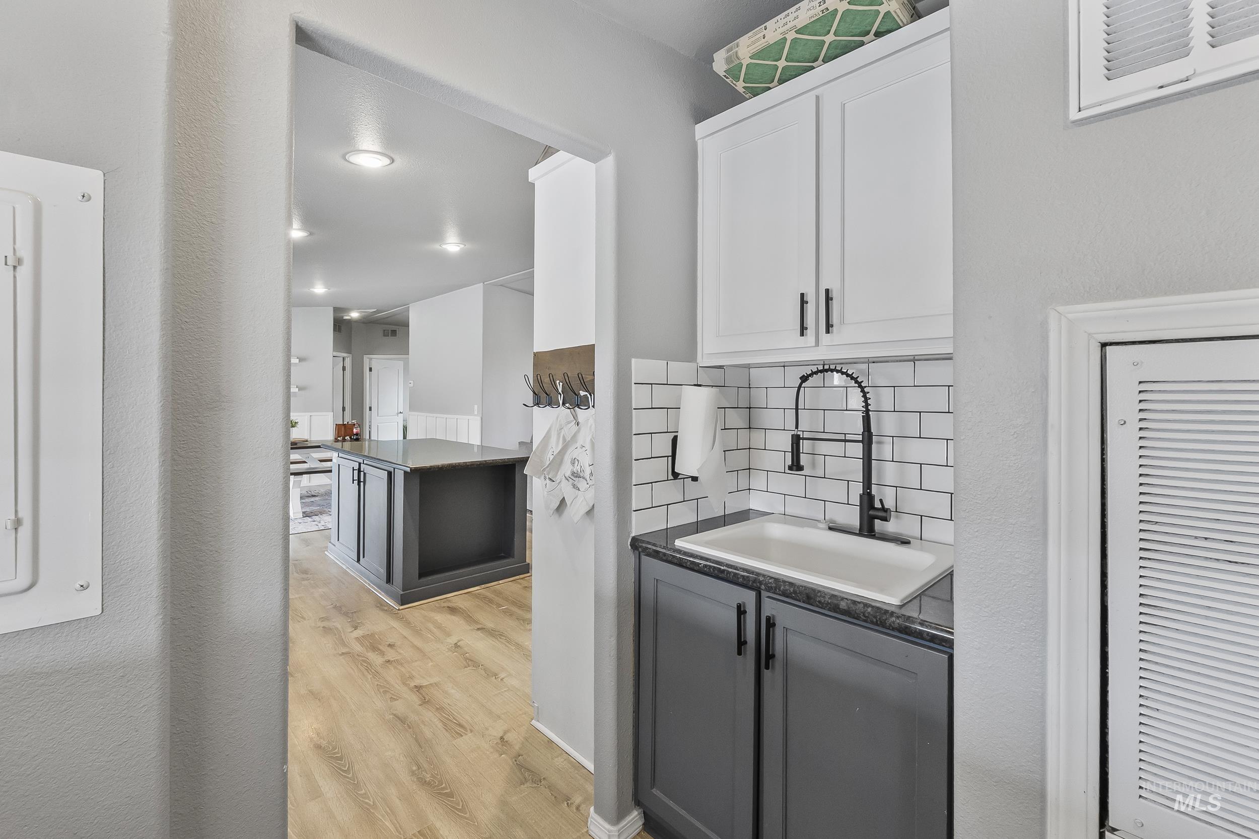 12944 Goodson Road Caldwell, ID 83607 - Photo 31 of 47 Bar with gray cabinets, light wood-style flooring, backsplash, white cabinetry, and dark stone countertops