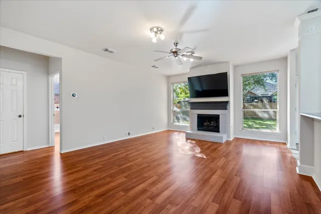 a view of an empty room with wooden floor and a ceiling fan