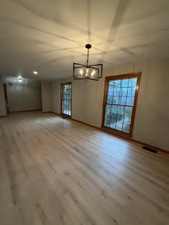 an empty room with wooden floor chandelier and windows