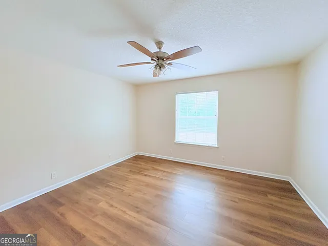 an empty room with wooden floor ceiling fan and windows