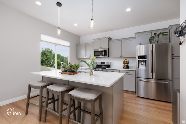 1654 South 730 West Provo, UT 84601 - Photo 9 of 33 Modern kitchen featuring light gray cabinetry, stainless steel appliances, a white island with seating for three, recessed lighting, and wood-finish flooring