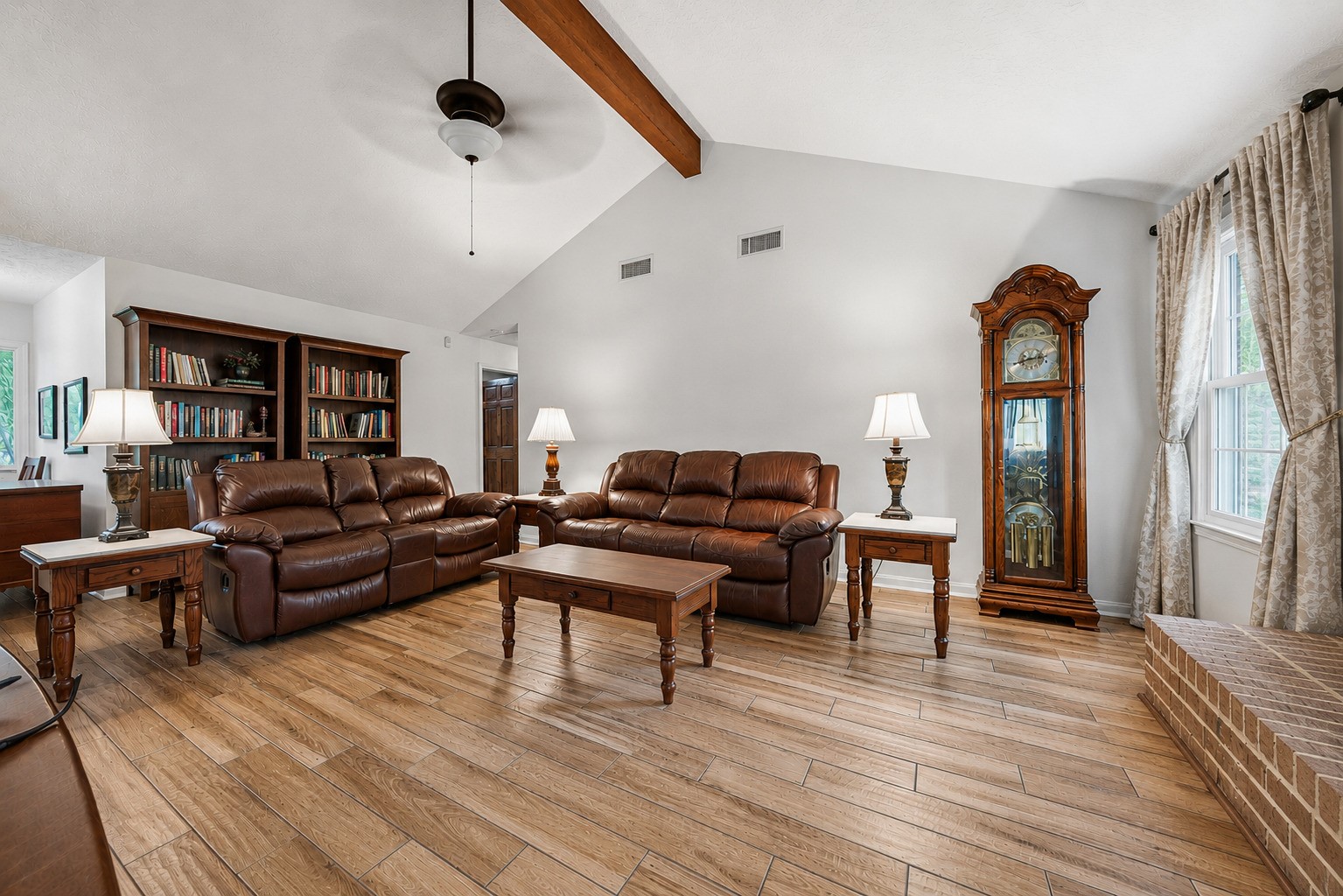 1004 Wagon Road Simonton, TX 77485 - Photo 8 of 40 The full scope of this generous living room is evident here, with vaulted ceilings, a ceiling fan, and wood-look tile flooring that extends throughout. Abundant wall space allows for flexible furniture arrangements, while the brick fireplace and large windows create a bright, cozy atmosphere.