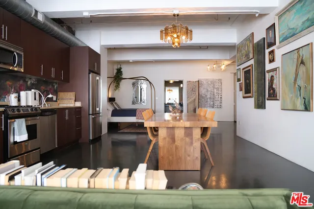 a kitchen with stainless steel appliances granite countertop a refrigerator a sink dishwasher a stove and a dining table with wooden floor