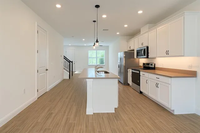 a kitchen with kitchen island a white counter top space a stove a refrigerator cabinets and wooden floor