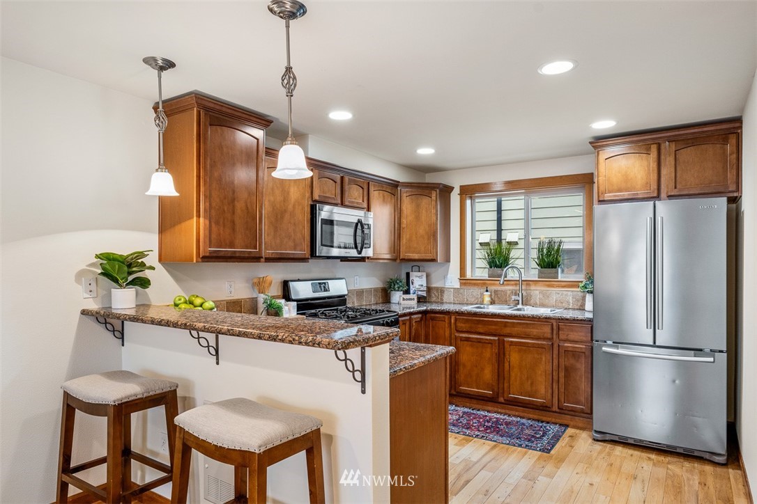 1122 North 92nd Street, Unit B Seattle, WA 98103 - Photo 9 of 32 a kitchen with stainless steel appliances granite countertop a refrigerator a sink dishwasher a stove and a dining table with wooden floor