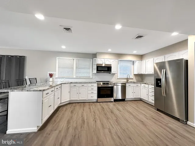 a kitchen with kitchen island granite countertop wooden floors and white cabinets