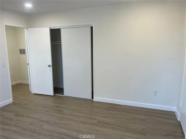 a view of an empty room with wooden floor and closet