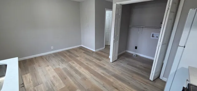 a view of an empty room with wooden floor and a hallway