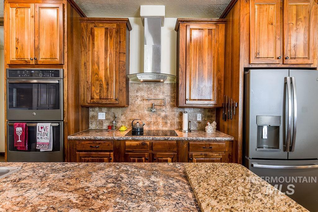 414 South Garfield Street Genesee, ID 83832 - Photo 11 of 50 Kitchen with stainless steel appliances, tasteful backsplash, wall chimney range hood, brown cabinets, and light stone counters