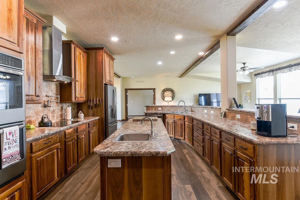 414 South Garfield Street Genesee, ID 83832 - Photo 12 of 50 Kitchen with a textured ceiling, brown cabinets, tasteful backsplash, dark wood finished floors, and wall chimney exhaust hood