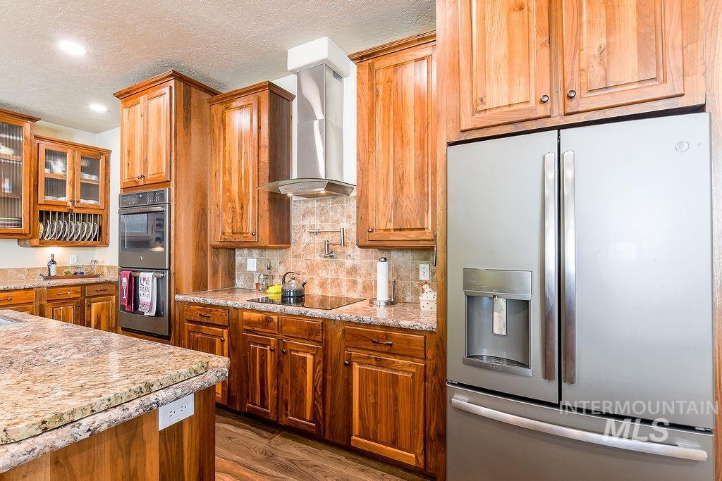 414 South Garfield Street Genesee, ID 83832 - Photo 10 of 50 Kitchen featuring stainless steel fridge with ice dispenser, tasteful backsplash, glass insert cabinets, brown cabinetry, and double oven