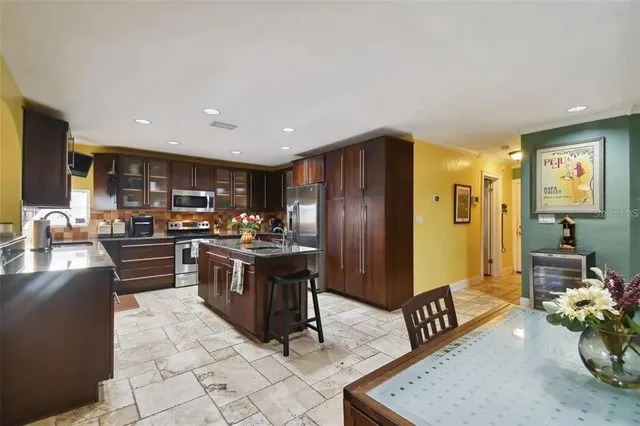 a kitchen with stainless steel appliances kitchen island granite countertop a refrigerator a stove a sink a dining table and chairs with the kitchen view