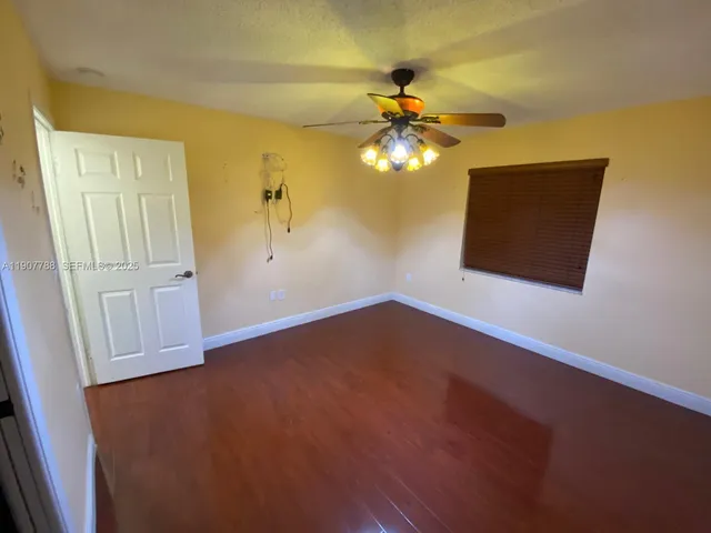 an empty room with wooden floor fan and windows
