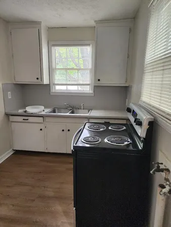 a kitchen with a stove a sink a window and cabinets