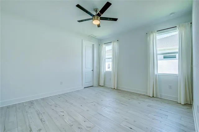 an empty room with wooden floor ceiling fan and windows