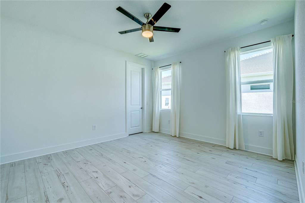 8218 Nevis Run Lakewood Ranch, FL 34202 - Photo 22 of 48 an empty room with wooden floor ceiling fan and windows