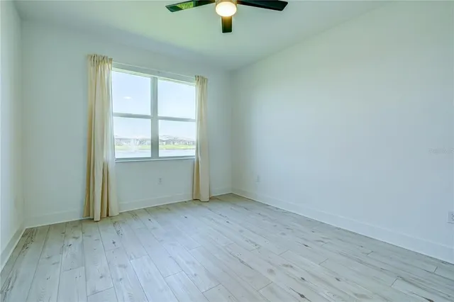 an empty room with chandelier fan and windows