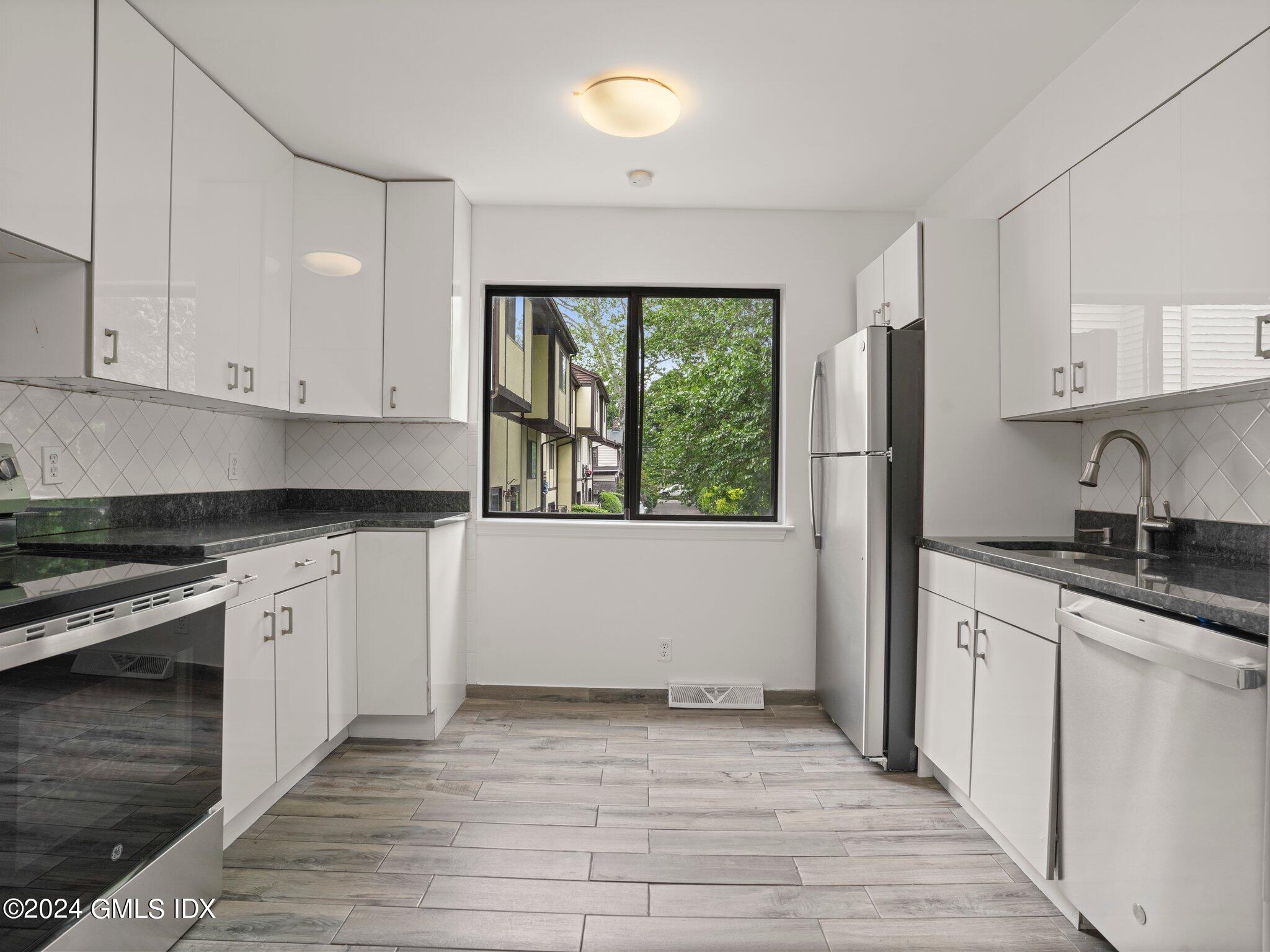 413 Glenbrook Road, Unit 1 Stamford, CT 06906 - Photo 1 of 21 a kitchen with granite countertop a stove a sink and white cabinets with wooden floor