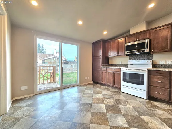 a view of kitchen with stainless steel appliances granite countertop a stove top oven a sink dishwasher a dining table and chairs with wooden floor