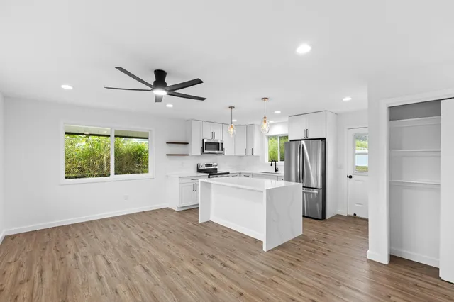 a kitchen with stainless steel appliances a stove top oven a refrigerator cabinets wooden floor and a window