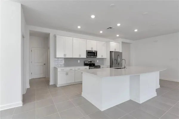 a large white kitchen with stainless steel appliances granite countertop a sink a stove a refrigerator and cabinets