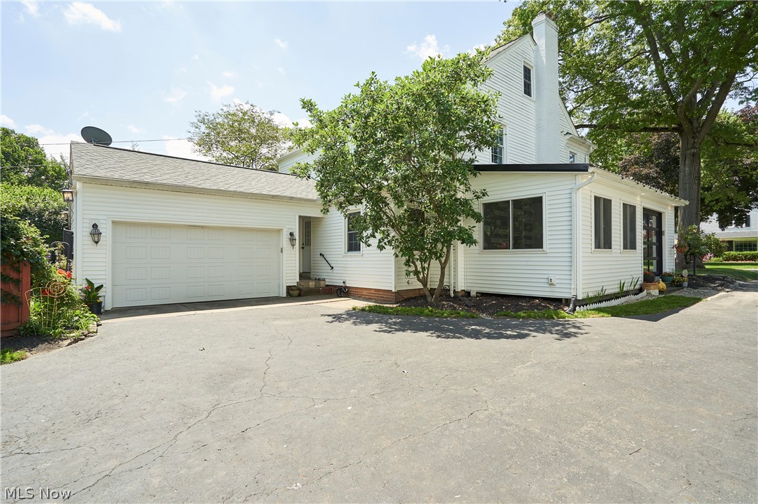 183 Overwood Road Akron, OH 44313 - Photo 29 of 34 White siding exterior featuring an attached garage with a white panel door, an enclosed porch with multiple windows, a prominent chimney, and mature landscaping